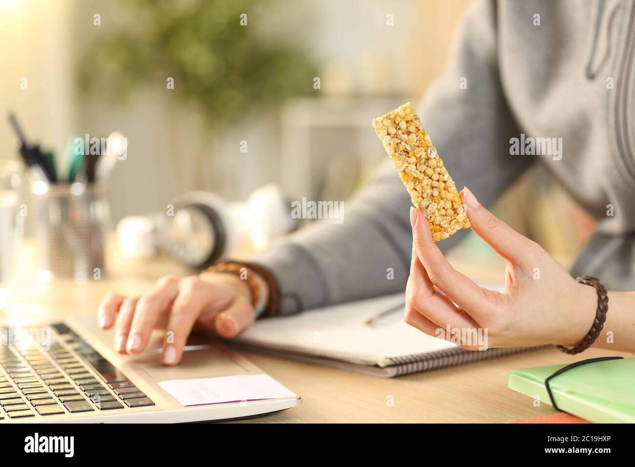 Close up of student girl hands holding snack bar using laptop at home Stock Photo