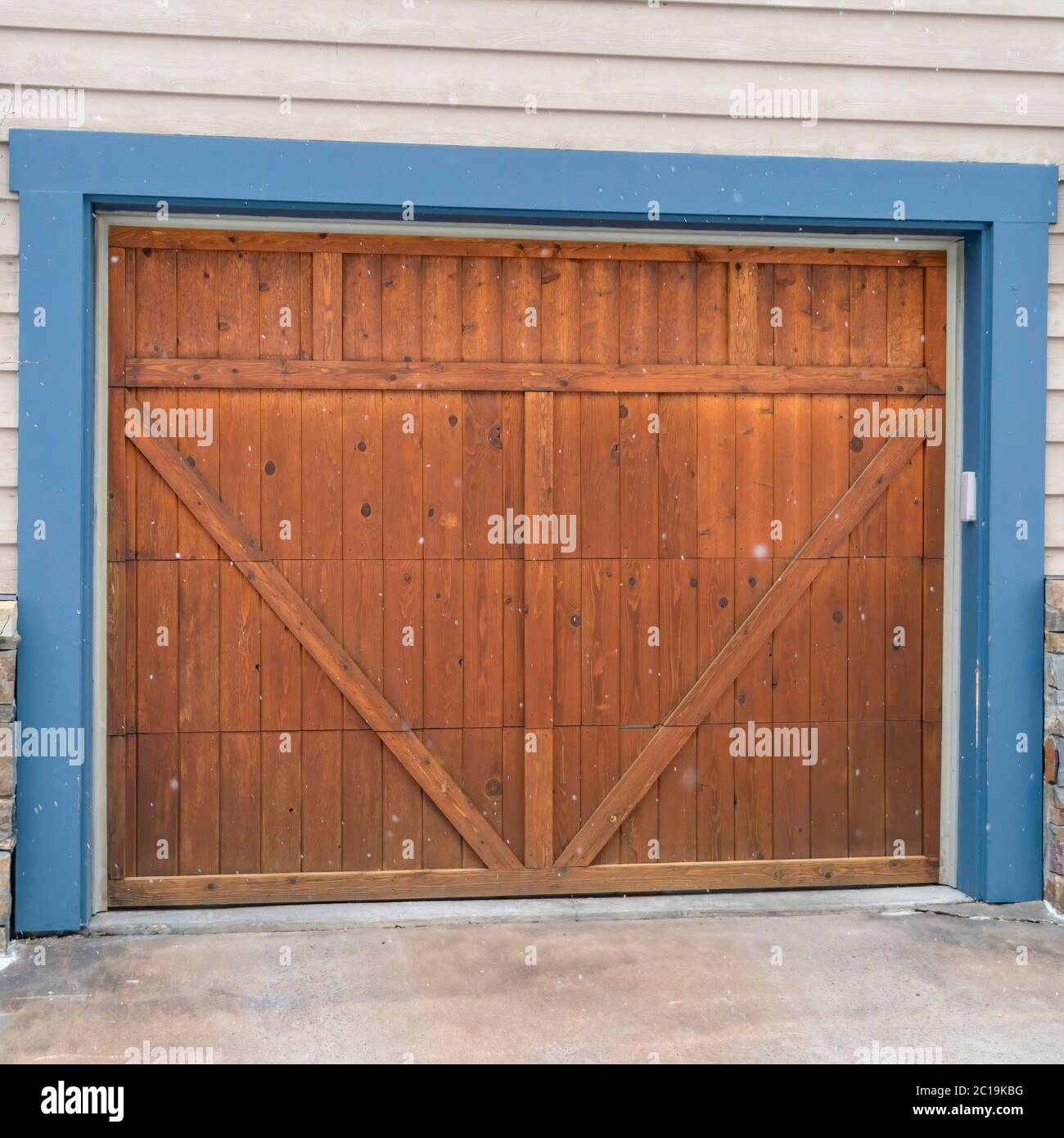 Square Brown wood garage door with blue frame flaned by wall mounted