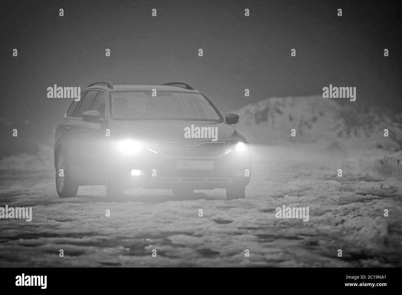 The greyscale photo of car with the lights on in the fog Stock Photo