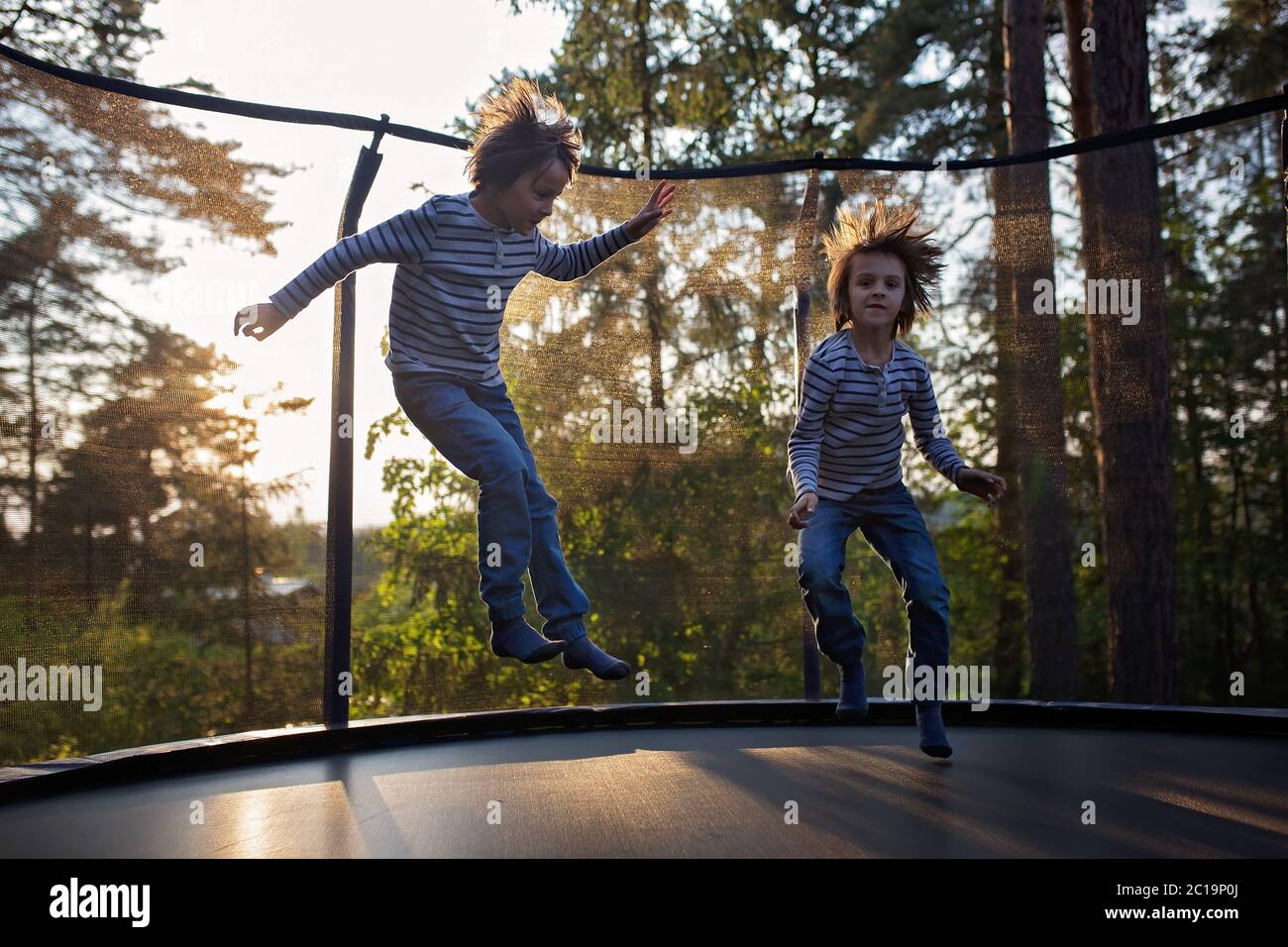 Sweet preteen boy jumping on trampoline making somersaults in the air. Child levitating. Happy child jumping on sunset Stock Photo