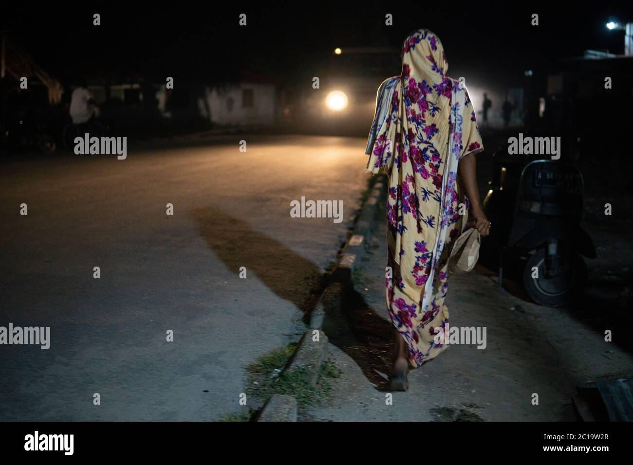 Woman Walking at night Along the Road in Traditional Muslim Women Cloth in Zanzibar, Tanzania Stock Photo
