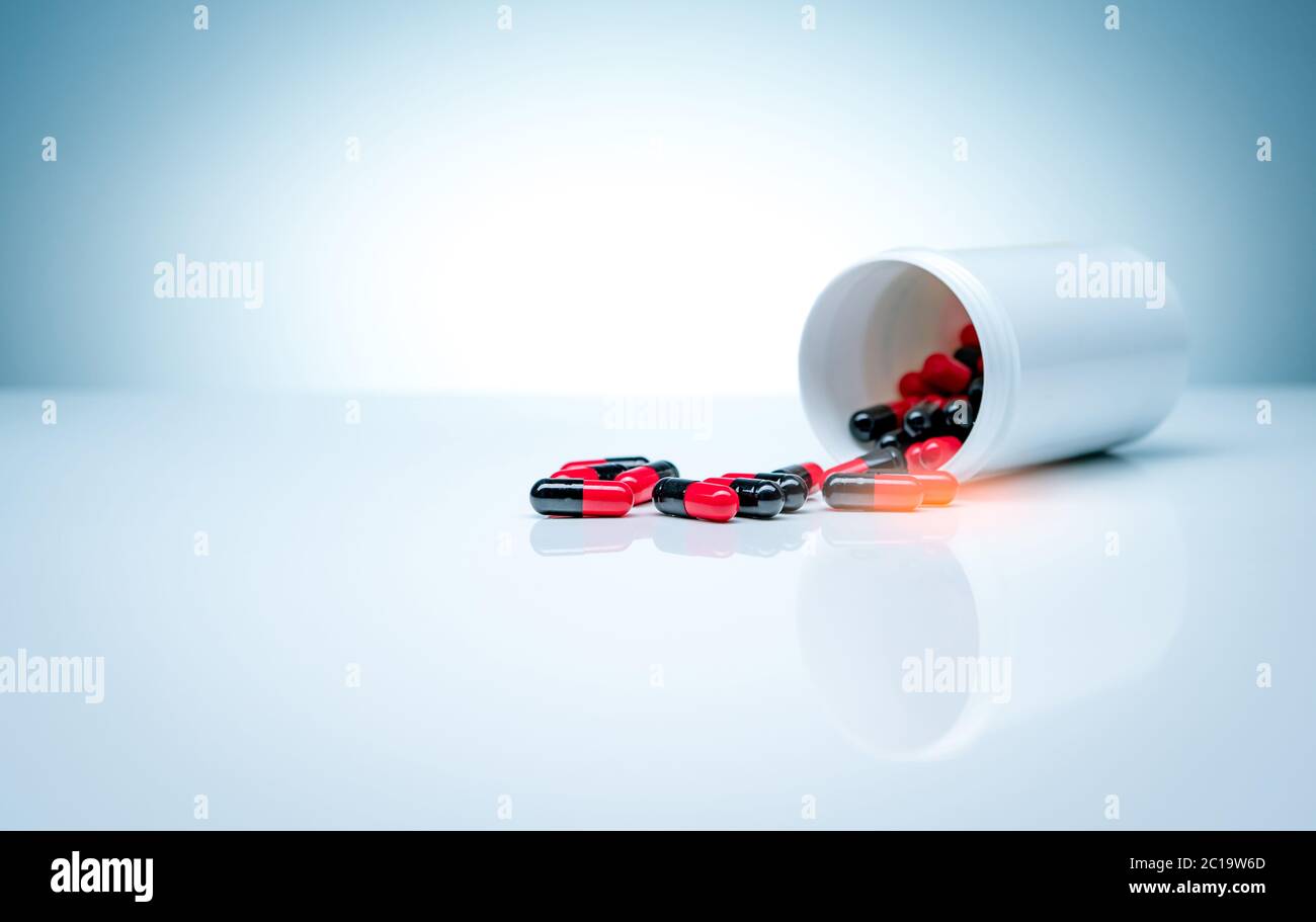 Red-black antibiotic capsule pills spread out of plastic drug bottle on white background. Pharmaceutical industry. Antibiotic drug resistance. Stock Photo