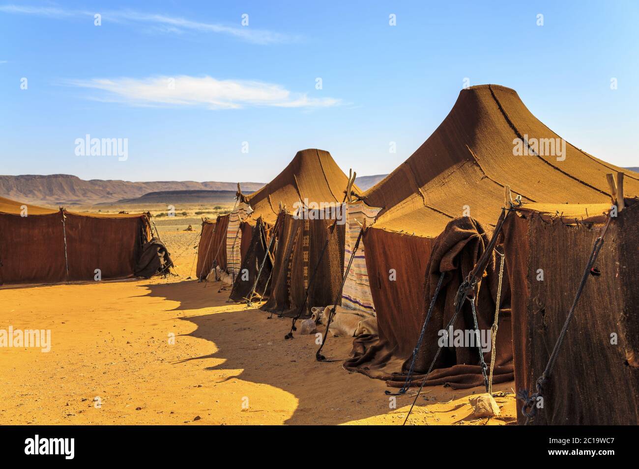 Tents in the middle of desert with mountains in the background, on a