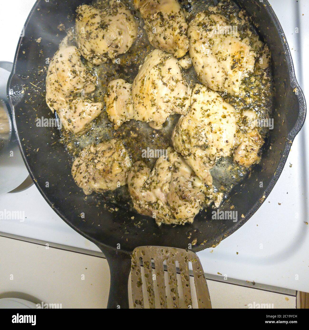 Square Slices of chicken meat with green herbs cooking on a hot cast iron skillet Stock Photo