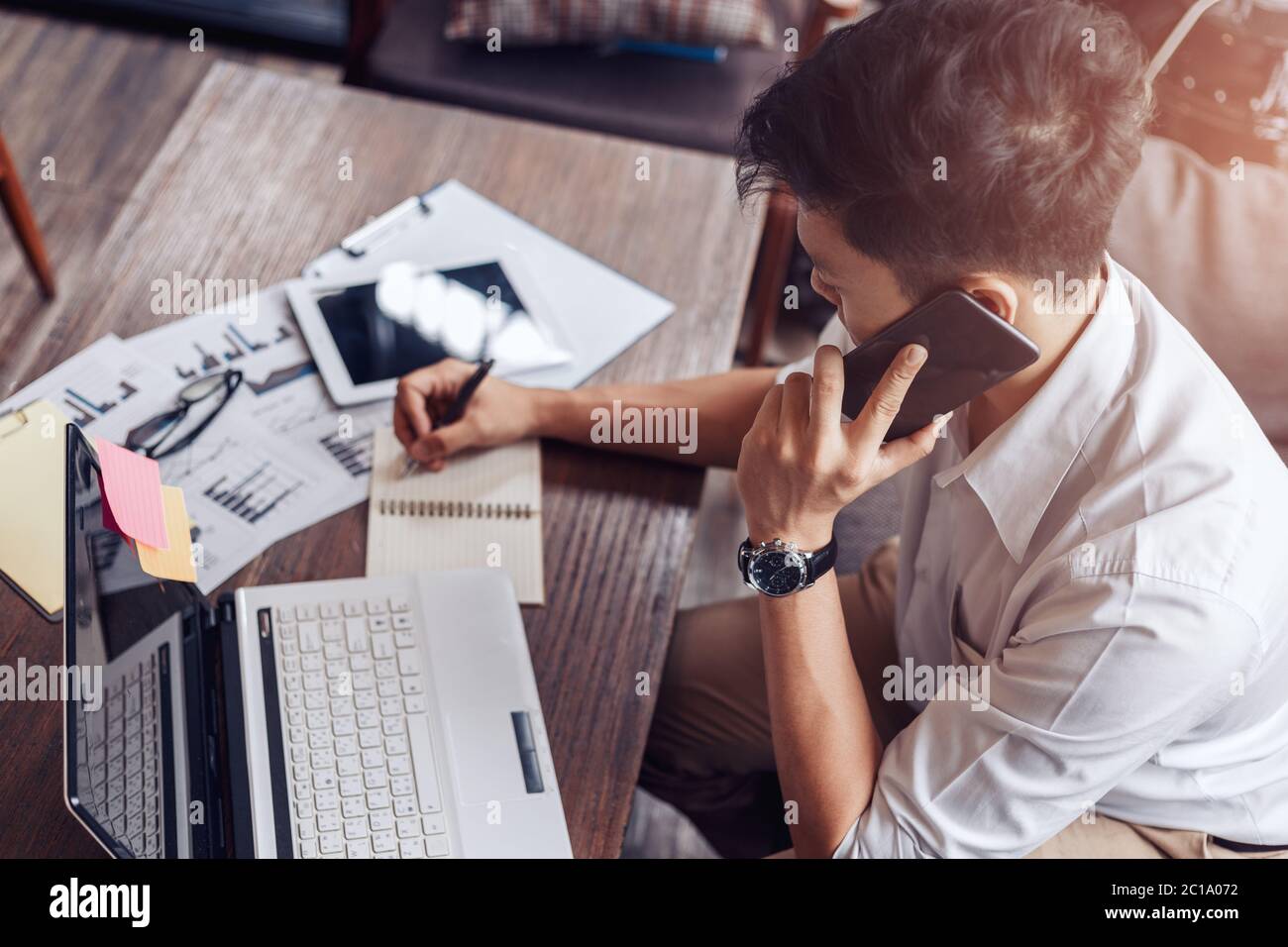 Businessman use mobile phone for talking and right hand use pen for checking data on paper chart, graph. Stock Photo