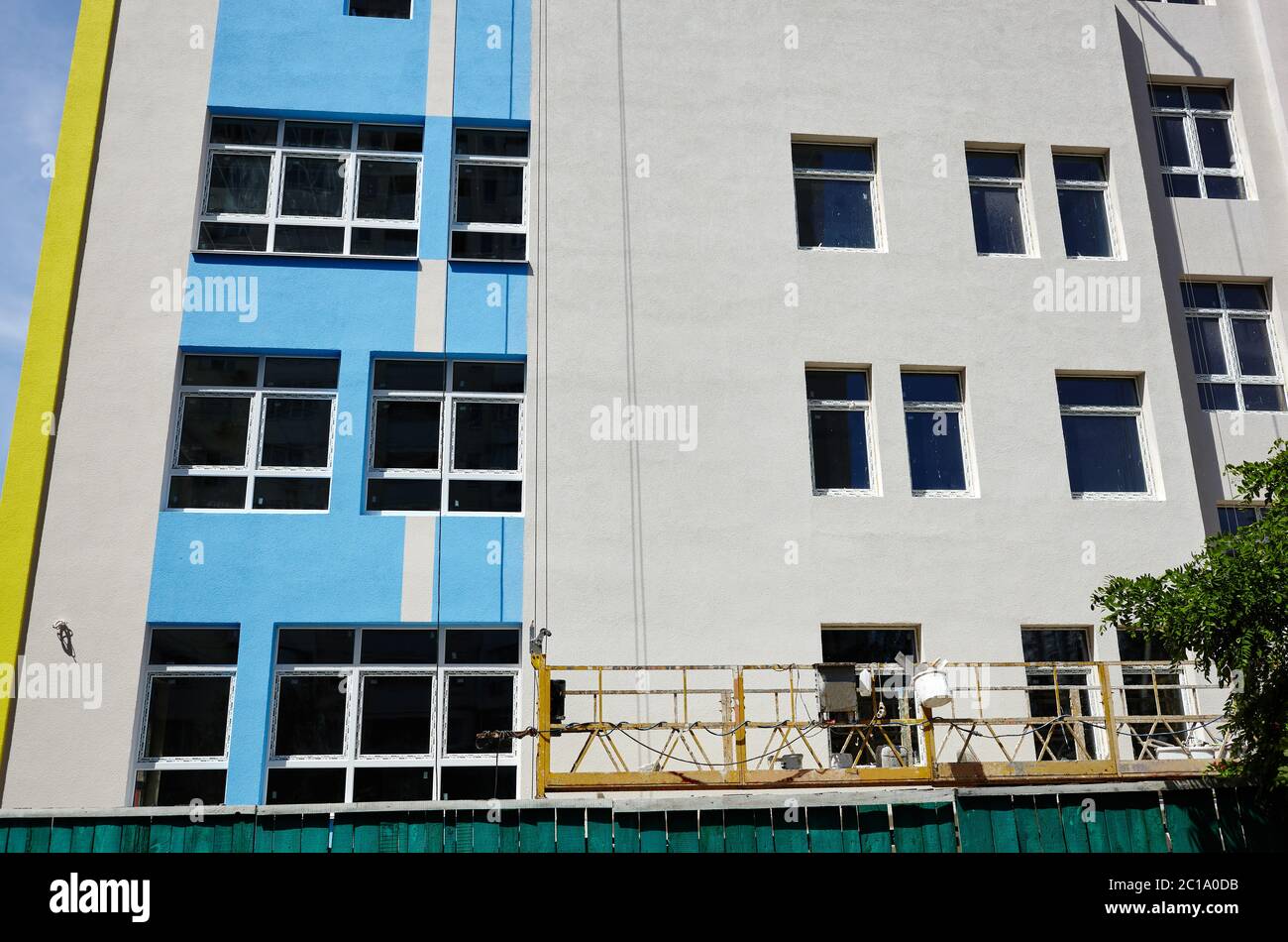 The progress of construction of the kindergarten building.Hanging scaffolding platform or window cleaning cradle system at construction site Stock Photo