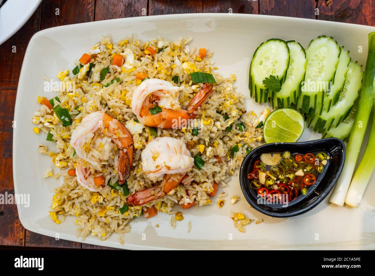 Top view of fried rice with shrimp, lemon, cucumber, onion and chili fish sauce in white plate. Stock Photo