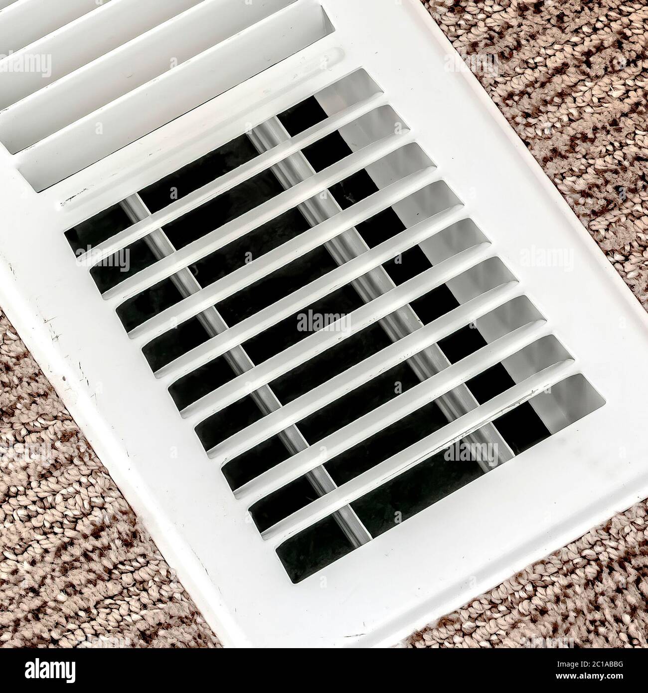 Square White air conditioner duct grille cover against floor with brown carpet Stock Photo