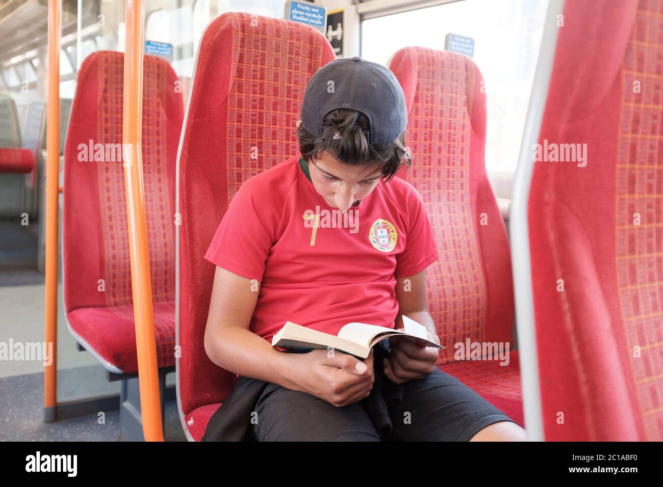 Young teenage boy, reads a book on deserted suburban train during coronavirus lockdown before the mandatory face covering rule, South Western Railways Stock Photo