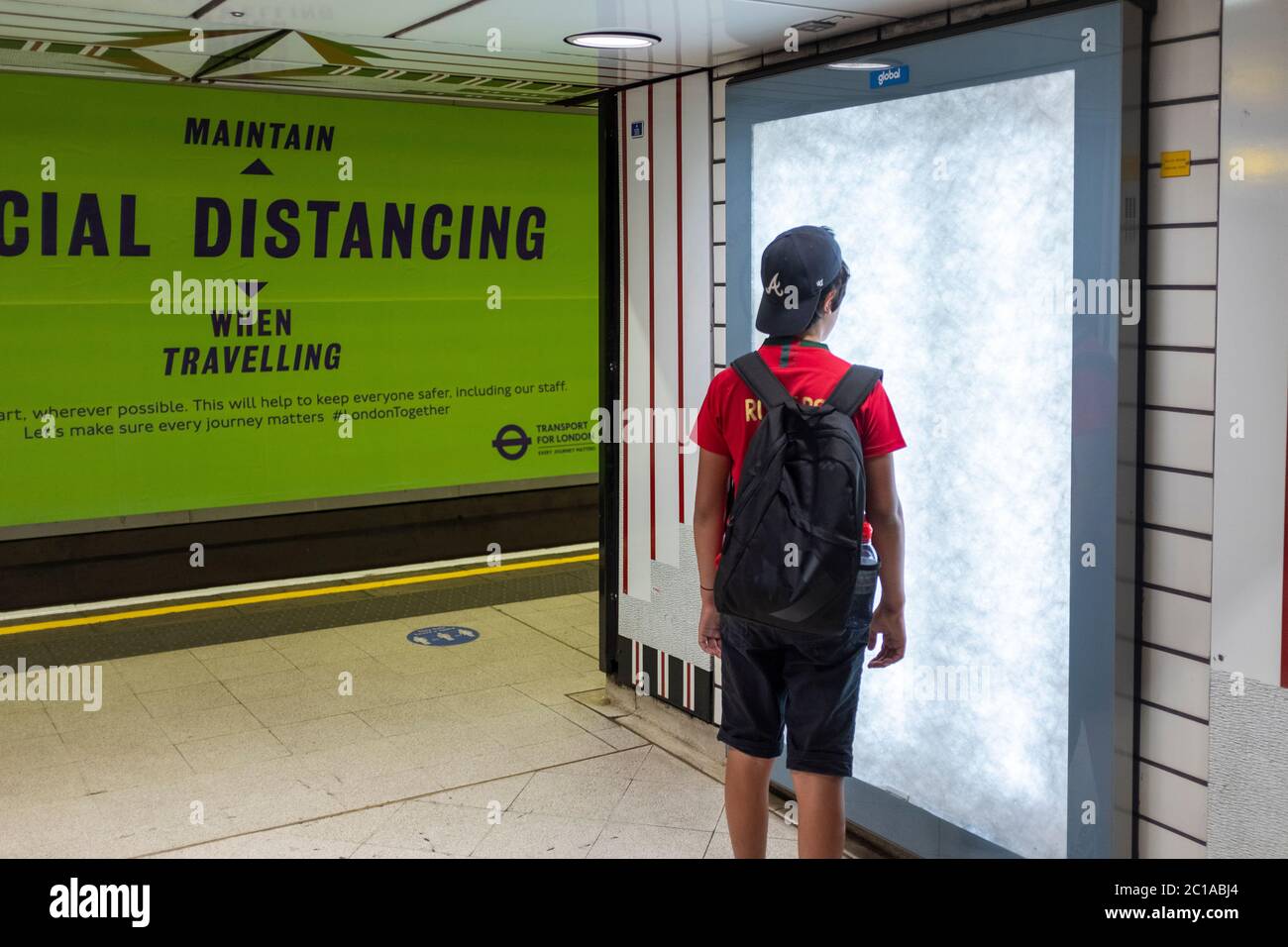 London, UK. 15th June, 2020. Coronavirus: Face coverings now mandatory on public transport. A young boy  travel on a tube.Social distancing billboard Stock Photo