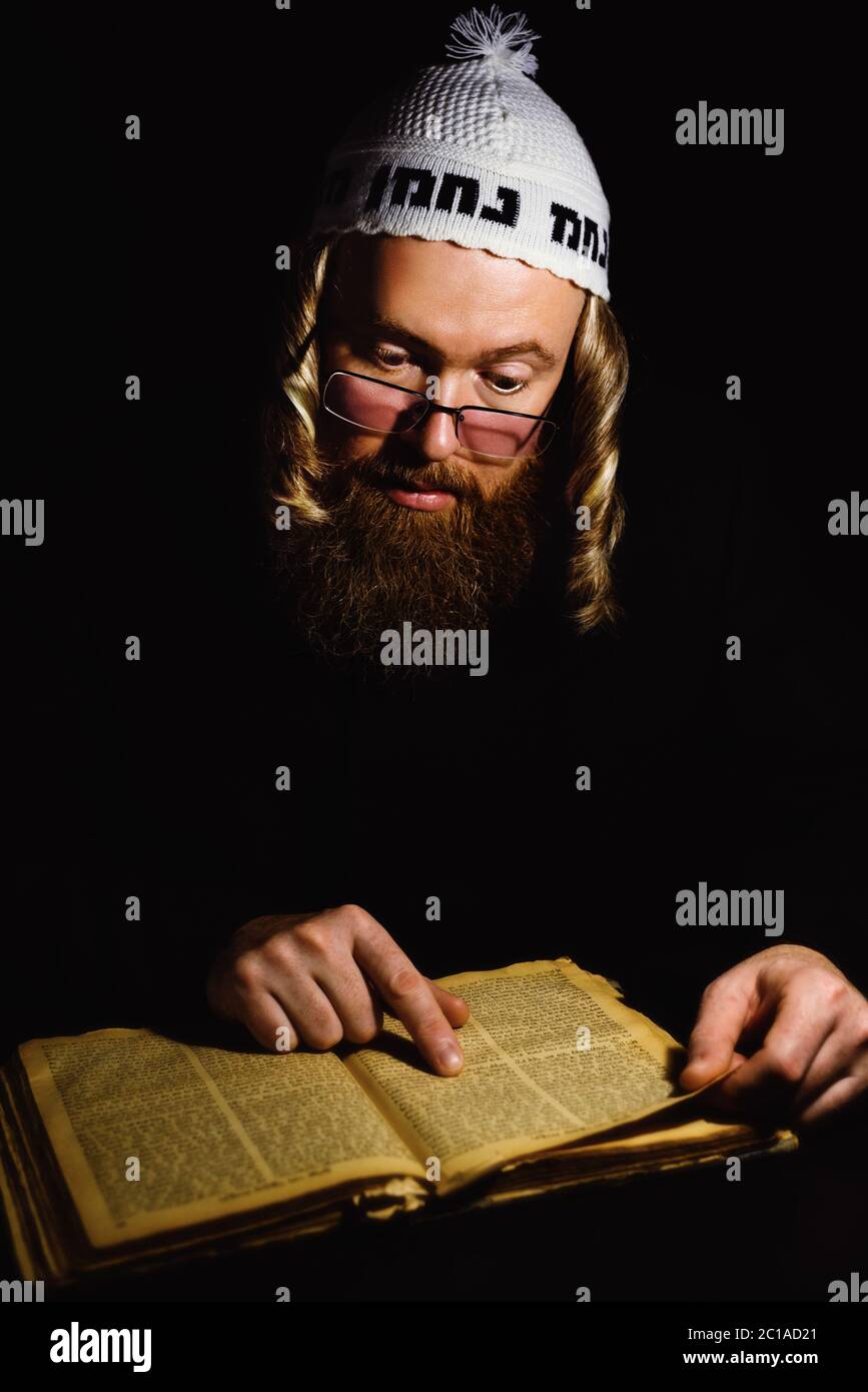 Hasidic jew reading Torah. Religious orthodox jew with sidelocks and red beard in white bale praying in the dark. Low key photo Stock Photo