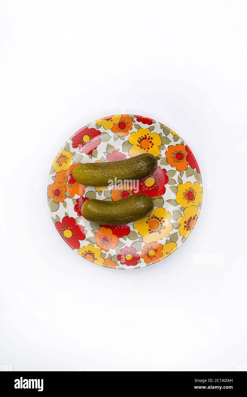 Overhead shot of on tow cucumbers on a flowery orange and red  dish, on white. Stock Photo