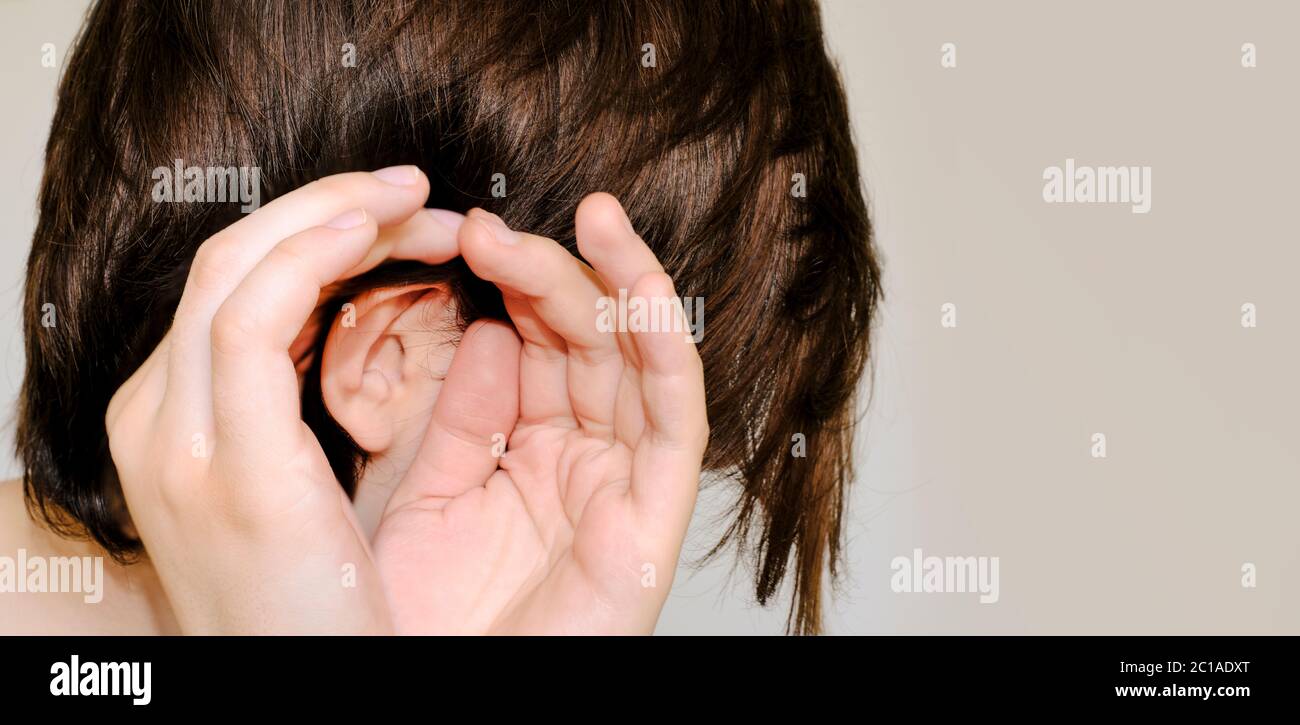 Gossip,rumors, whisper, hearing concept. Young Woman putting hand ear to hear better. Studio shot on grey background. Close-up,copy space Stock Photo