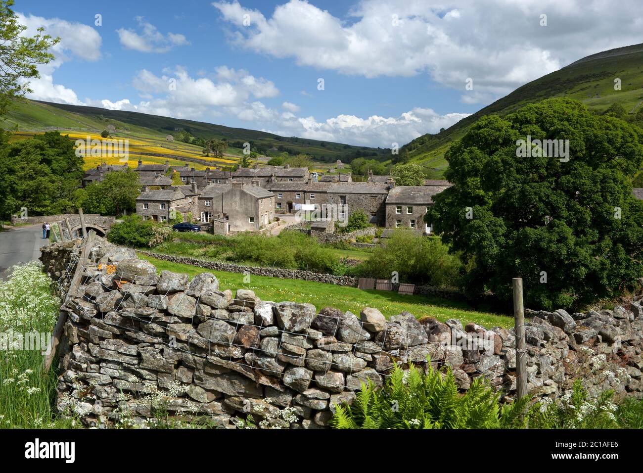 View over traditional dry stone wall to village of Thwaite in Swaledale valley, Thwaite, Yorkshire Dales National Park, North Yorkshire, England, UK Stock Photo
