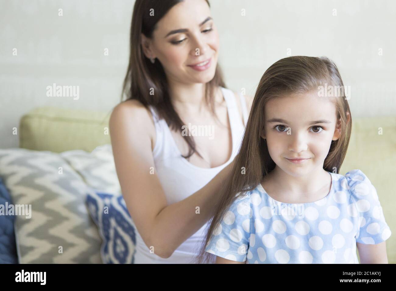 Adorable young family in living room. Mother combing her daughter's hair Stock Photo