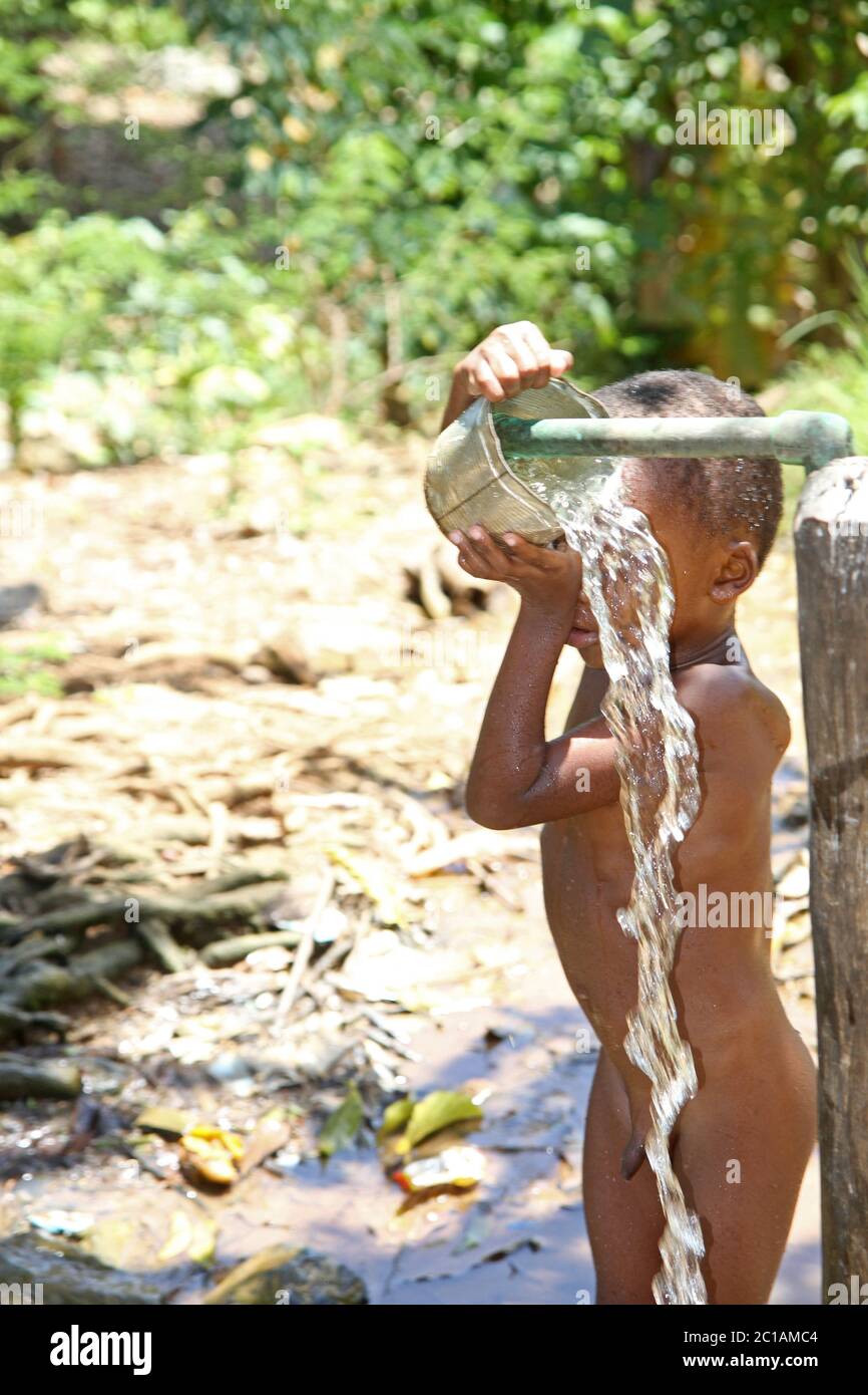 Young African boy having a bath with tap and bucket, Ampangorinana Village, Nosy Komba Island