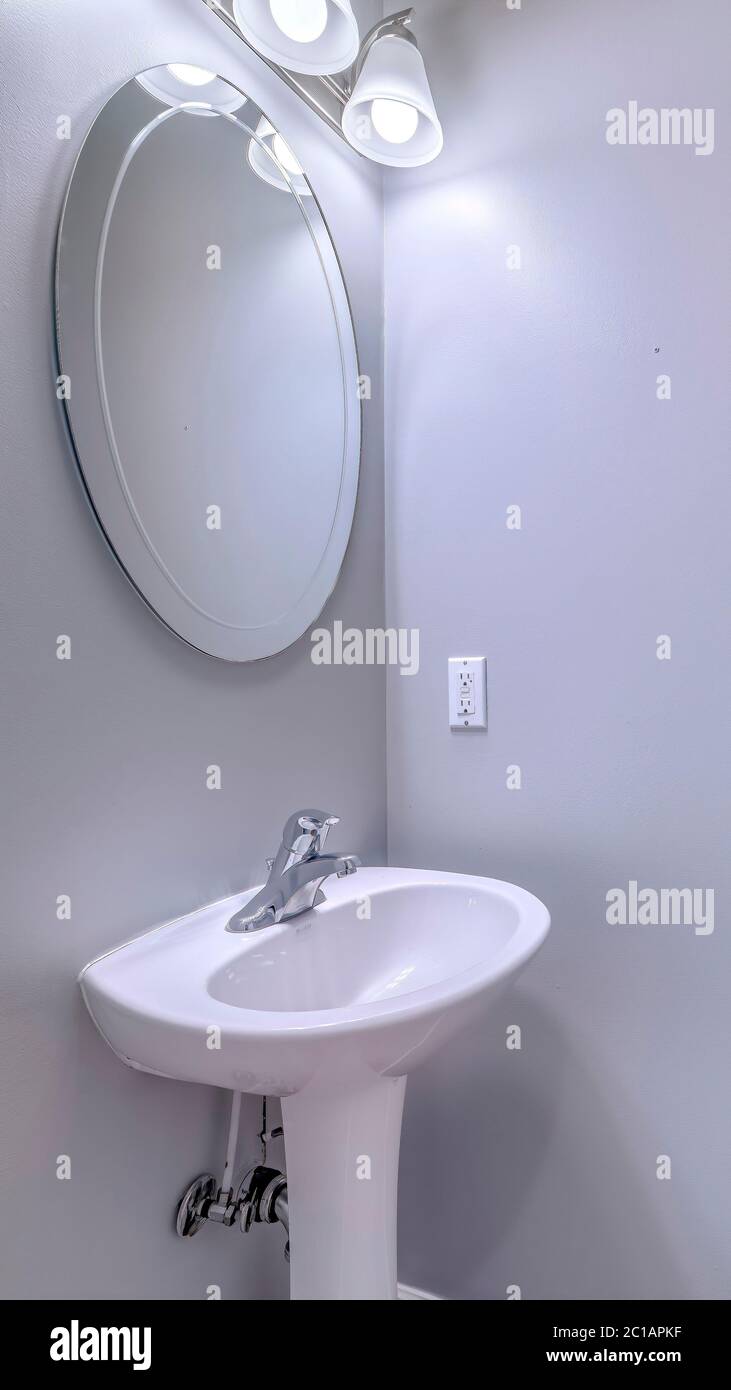 Vertical Bathroom interior with wall light and oval mirror over stand alone pedestal sink Stock Photo