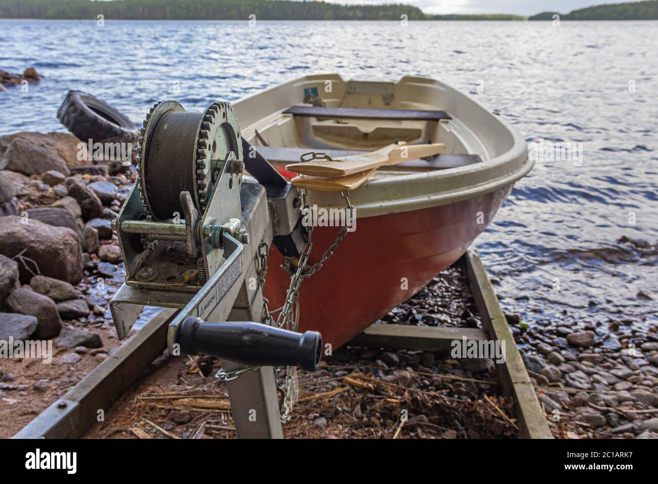 A red rowing boat (oar boat) on a slipway with a winch on lake shore in Finland Stock Photo