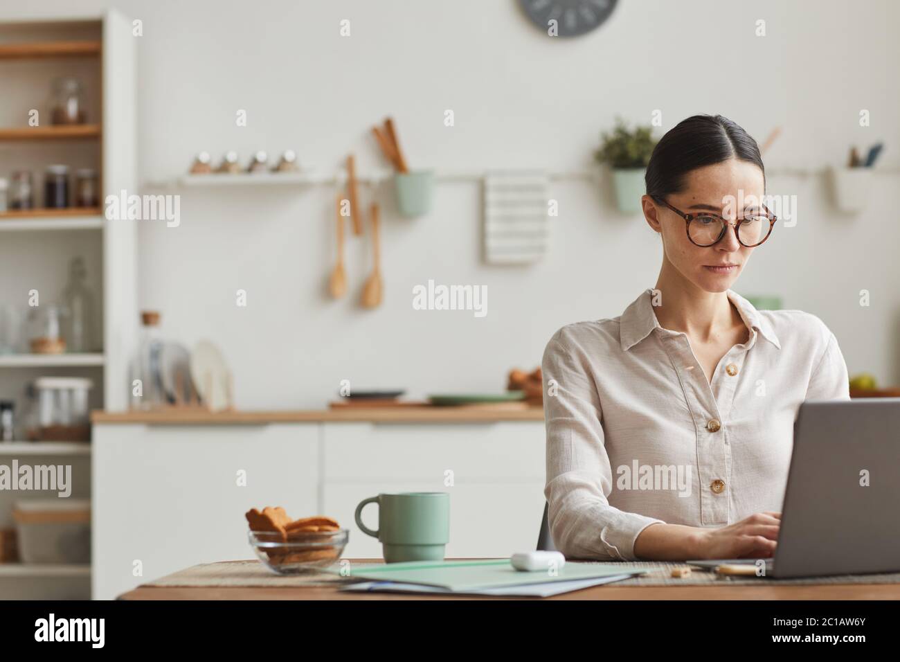 Portrait of elegant young woman wearing glasses while using laptop at cozy home office workplace, copy space Stock Photo