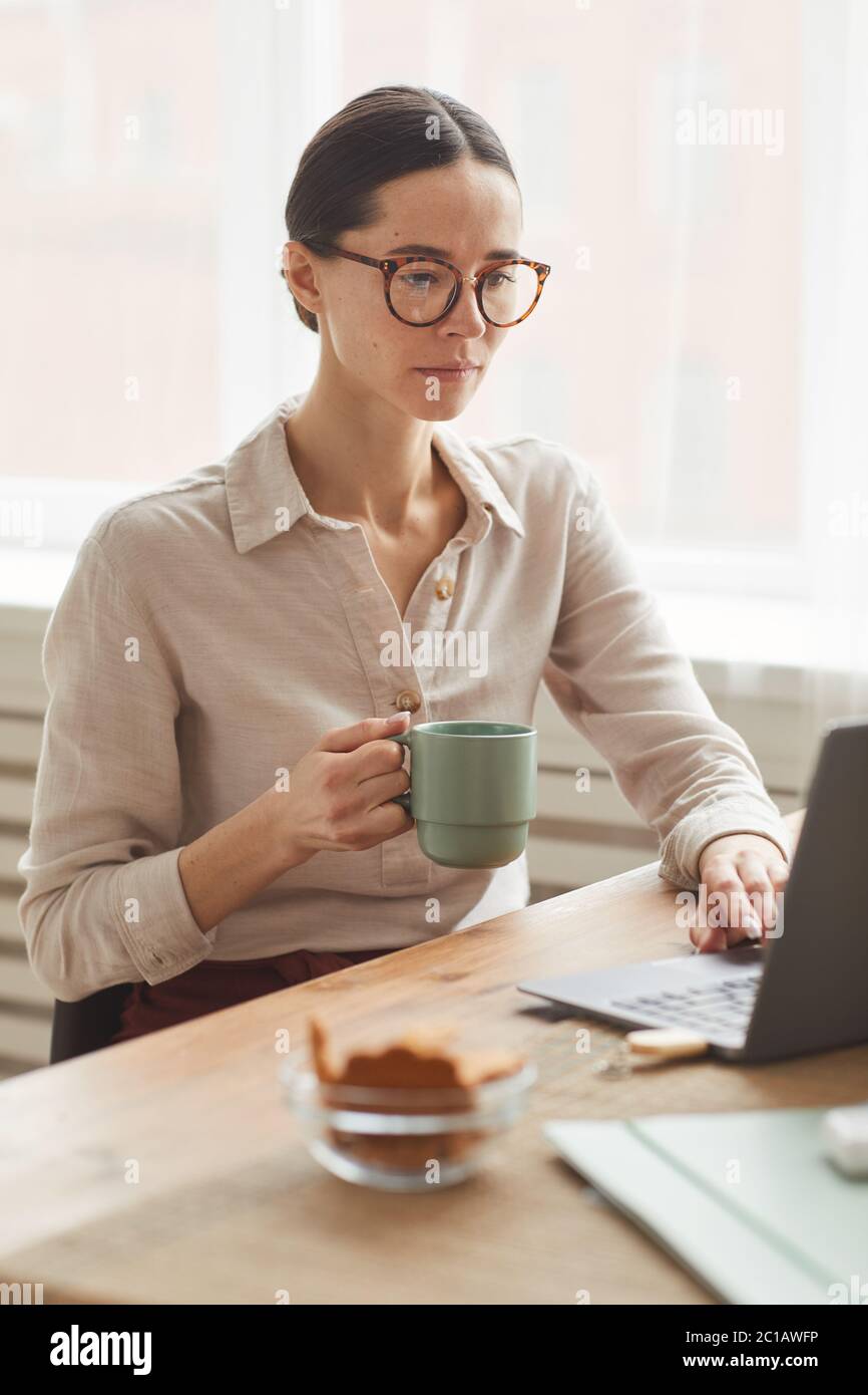 Vertical portrait of elegant businesswoman wearing glasses while using laptop at cozy home office workplace Stock Photo