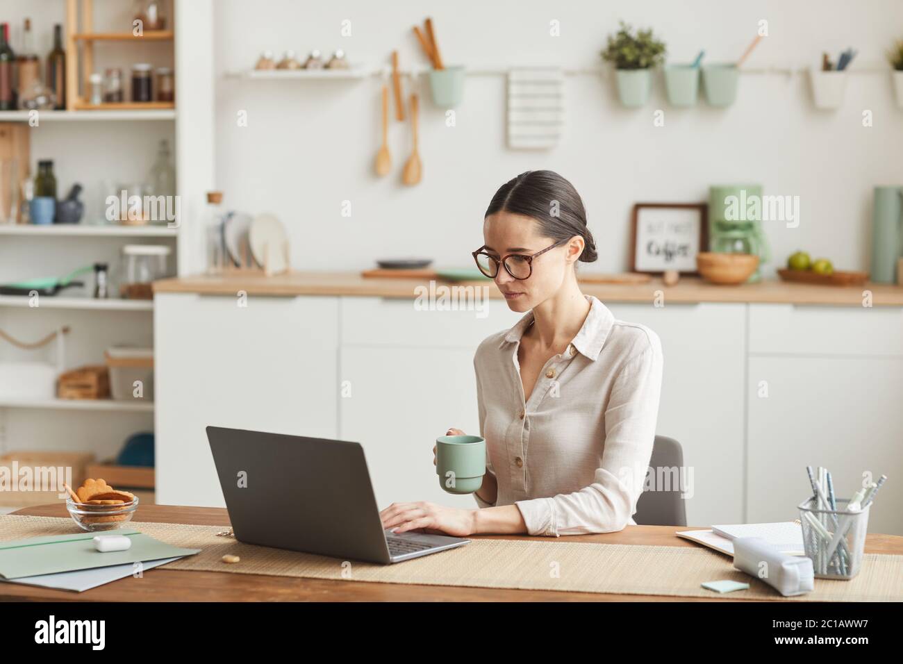 Portrait of elegant businesswoman drinking coffee while using laptop at cozy home office workplace, copy space Stock Photo