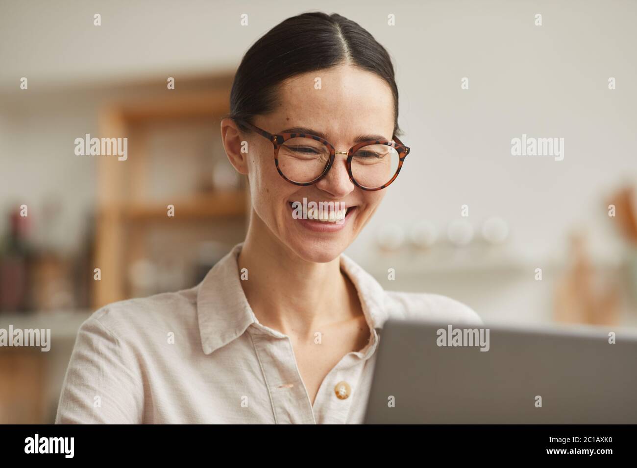 Warm-toned portrait of young businesswoman wearing glasses smiling happily while looking at laptop screen, copy space Stock Photo