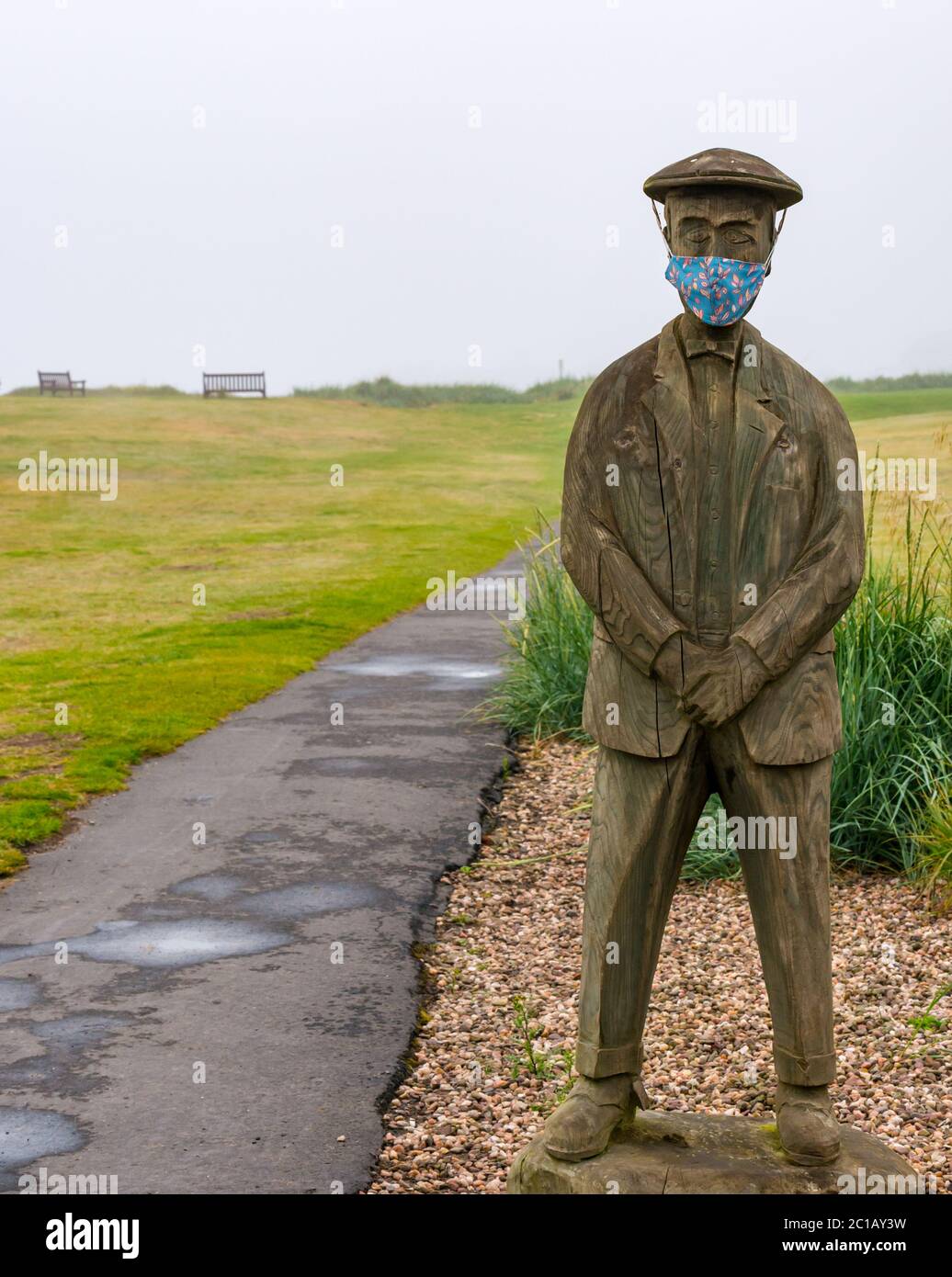 North Berwick, East Lothian, Scotland, United Kingdom, 15th June 2020. UK Weather: thick fog continues for the 3rd day in East Lothian with few people in the popular seaside town. A wooden statue of Ben Sayers, a 19th century professional golf player by Ed Robinson, has acquired a colourful face mask on Rotary Way on Elcho Green Stock Photo