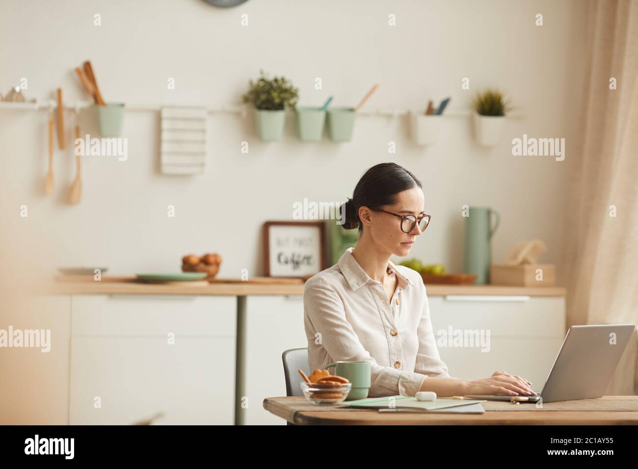 Warm-toned side view portrait of elegant young woman wearing glasses while using laptop at cozy home office workplace, copy space Stock Photo