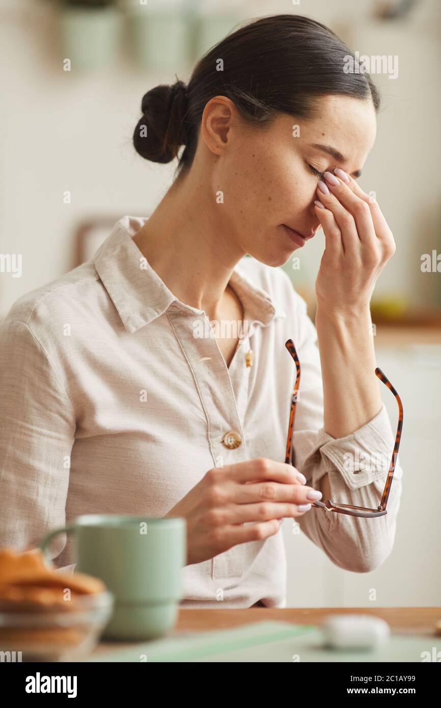 Vertical warmtoned portrait of tired young woman rubbing nose bridge
