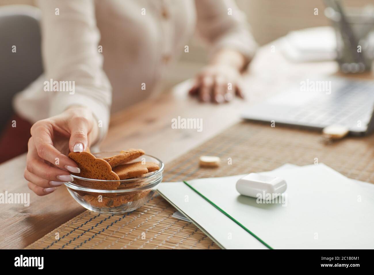 Warm-toned close up of unrecognizable woman taking homemade cookie while working at home, copy space Stock Photo