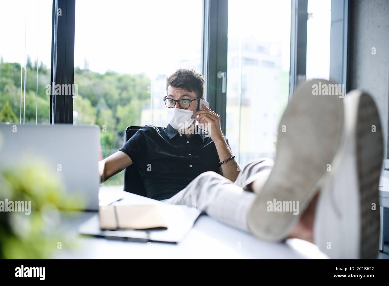 Young man with face masks back at work or school in office after lockdown, having fun. Stock Photo