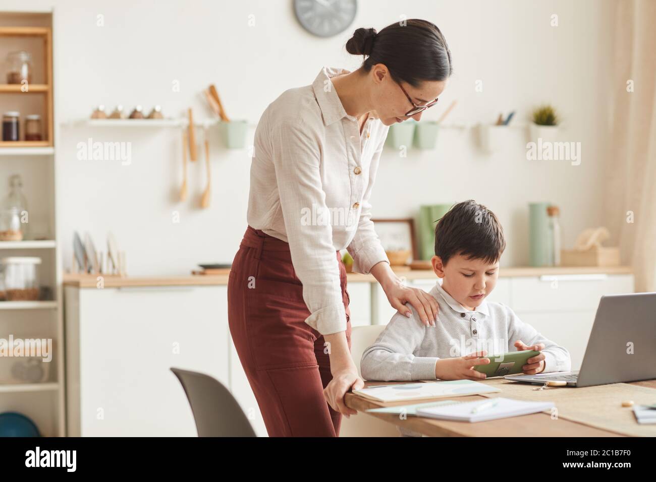Warm-toned portrait of young mother helping boy trying to study at home in cozy interior, copy space Stock Photo