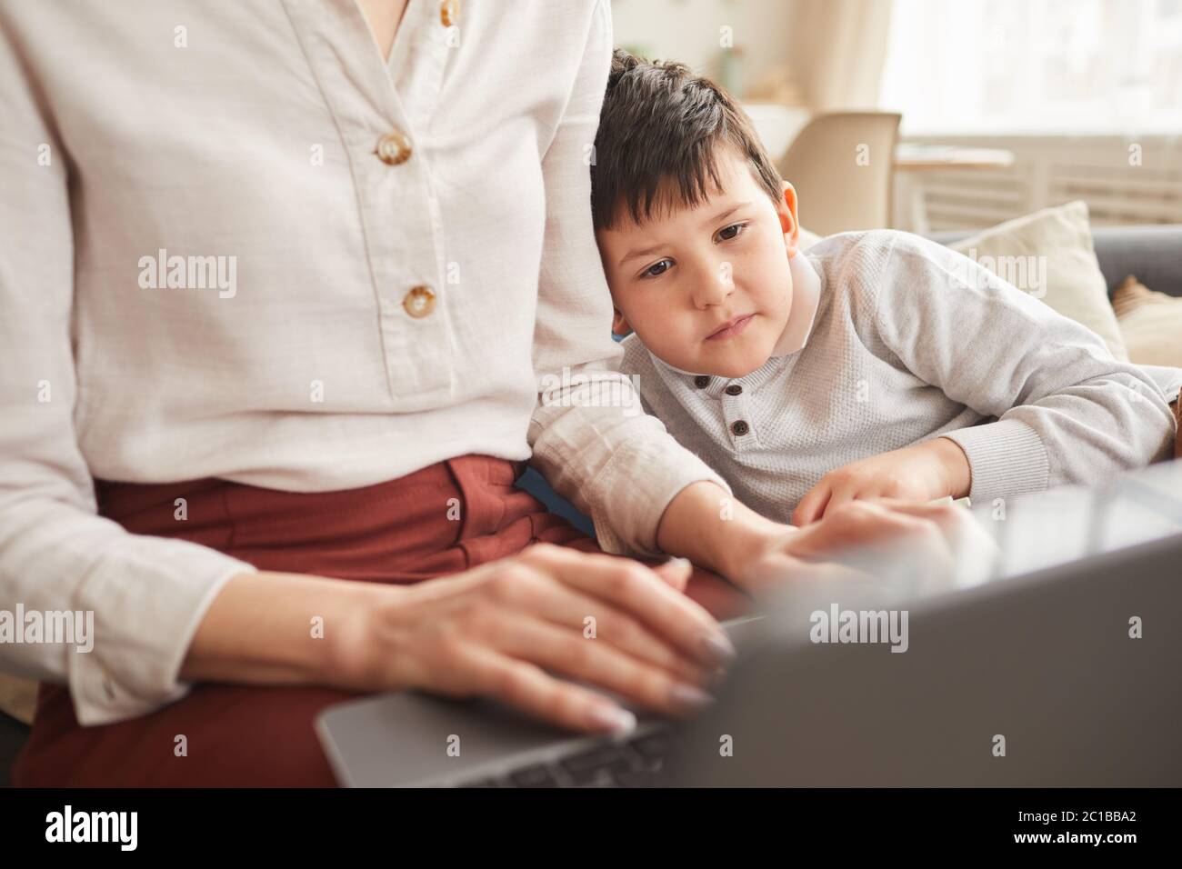 Close up portrait of cute boy looking at laptop screen while studying at home with mother helping him in cozy interior, copy space Stock Photo