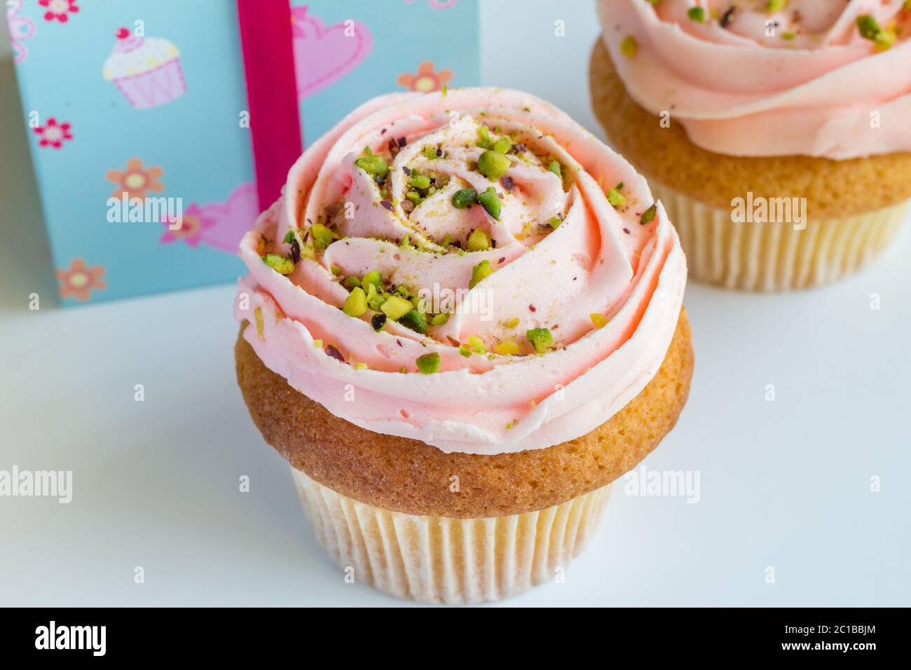 Two peach rose swirled frosted cup cakes with pistachio nut sprinkles