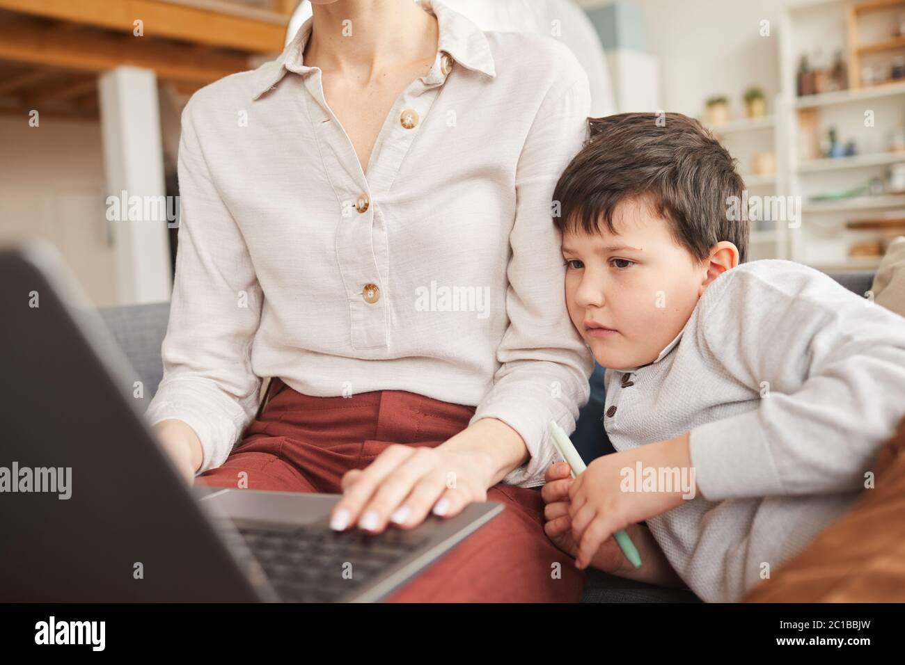 Close up portrait of boy looking at laptop screen while studying at home and leaning on mom in cozy interior, copy space Stock Photo