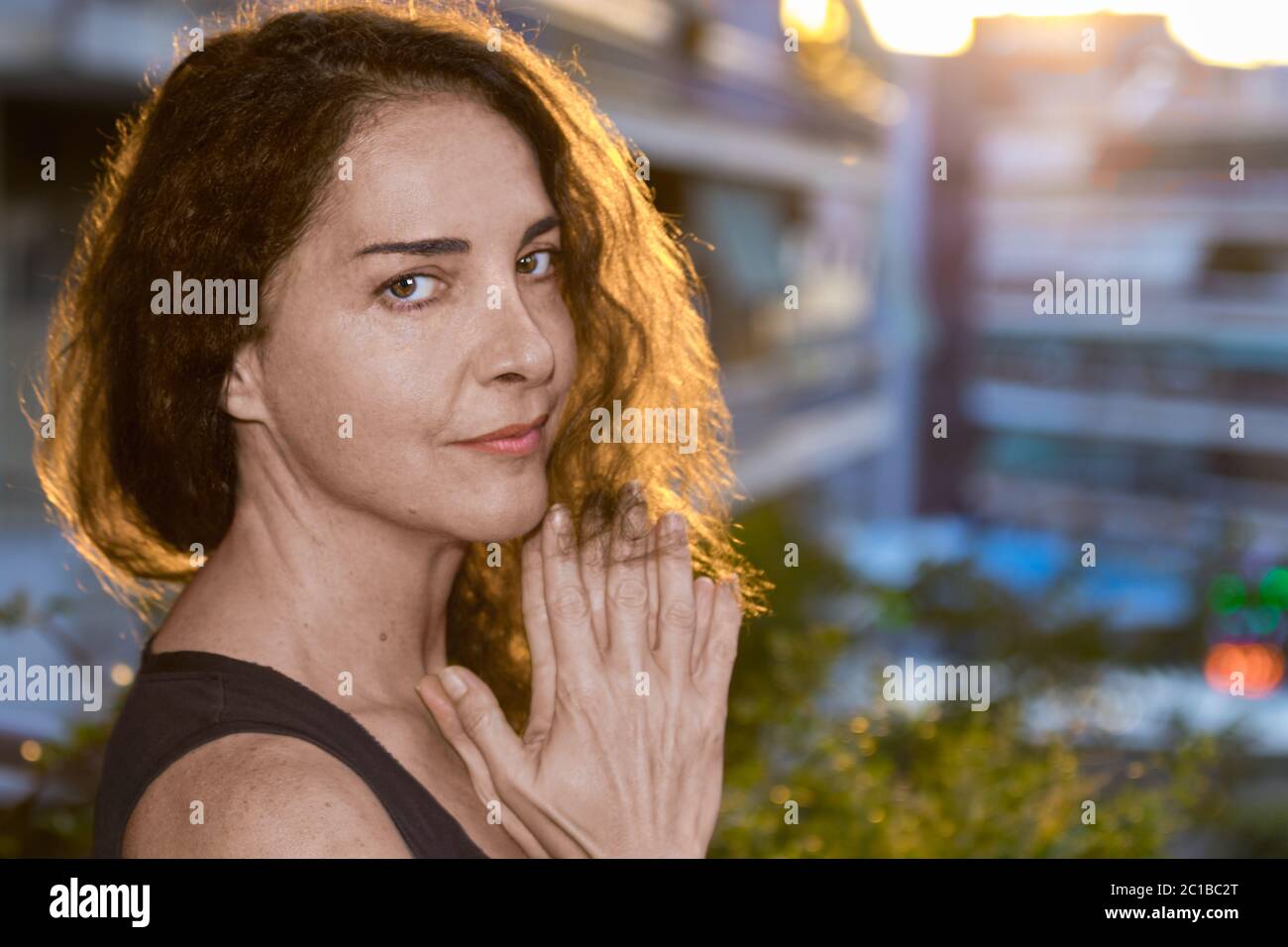 Portrait of attractive mature woman looking camera aside, holding hands together under her chin. Stock Photo