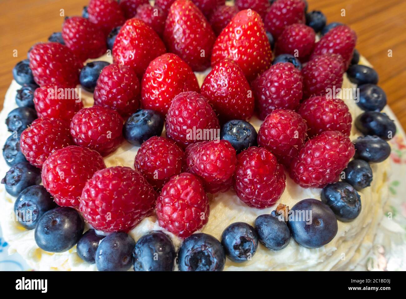 A cake decorated with butter icing and summer fruits including strawberries, raspberries and blueberries. Stock Photo