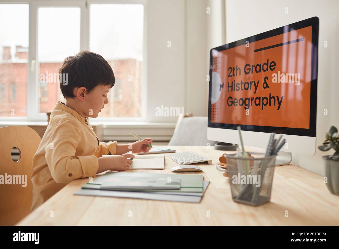 Warm-toned side view portrait of cute little boy studying at home while sitting at desk by computer with online school website, copy space Stock Photo