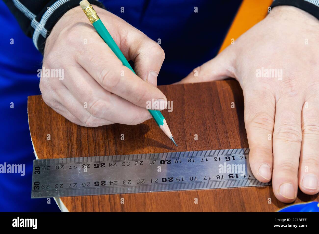 Close-up Men's hands draw a pencil on the ruler with a sub-standard template for cutting out furniture details next to the jigsa Stock Photo