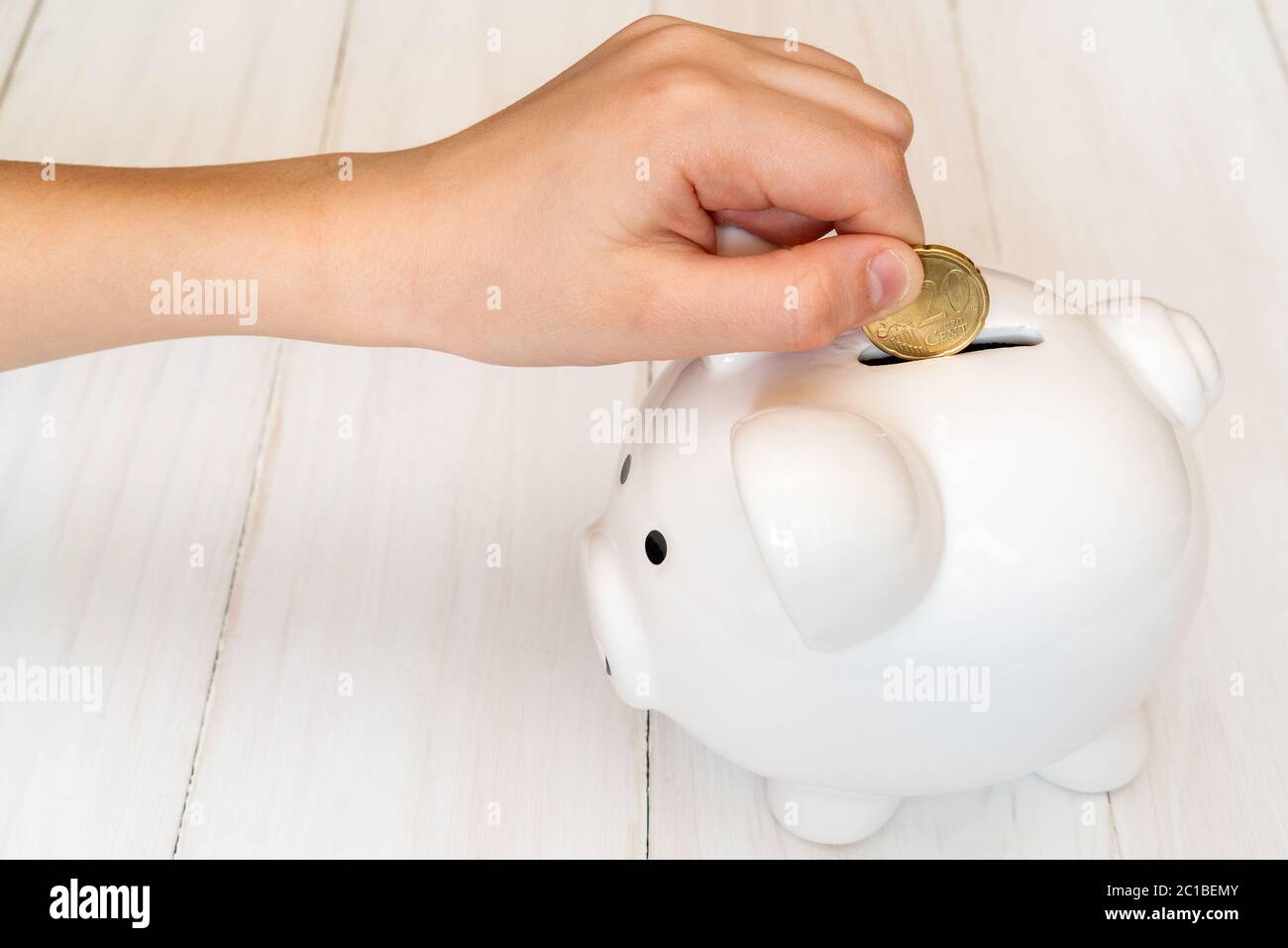 Child's hand putting a coin into piggy bank Stock Photo - Alamy