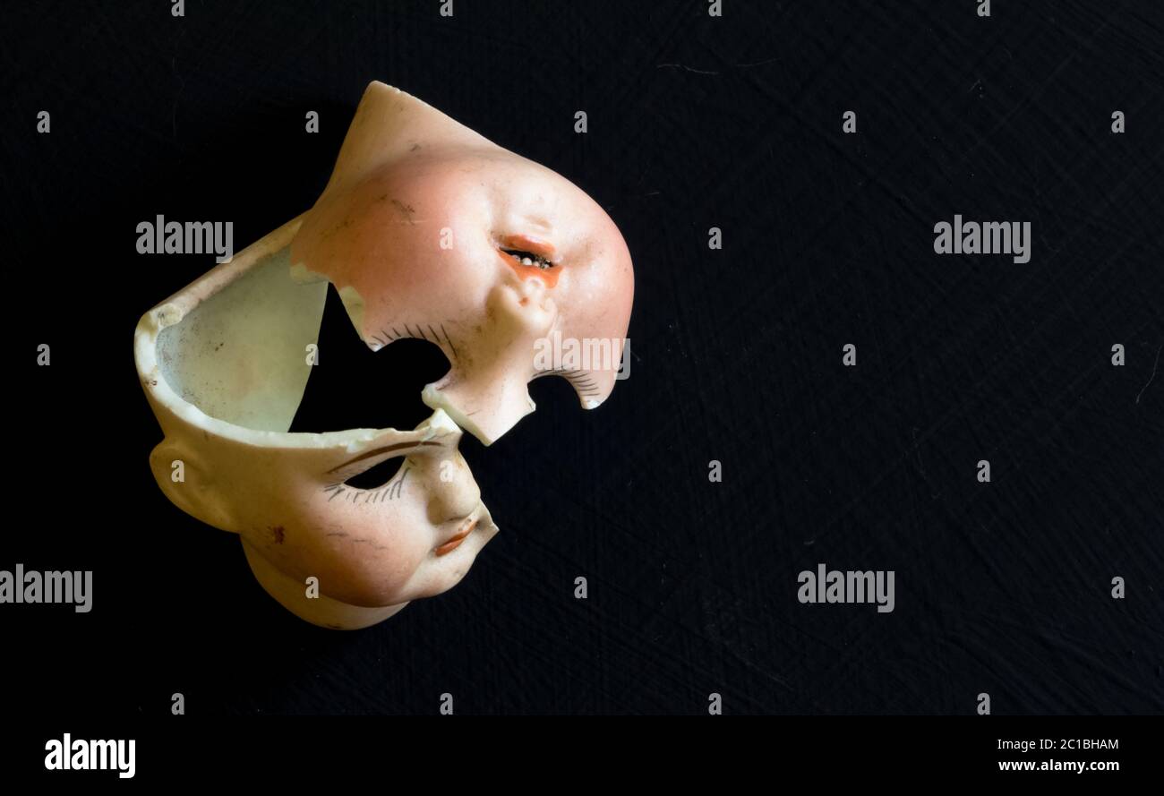 Broken doll face on black background. Conceptual image with two broken ceramic doll faces. Stock Photo