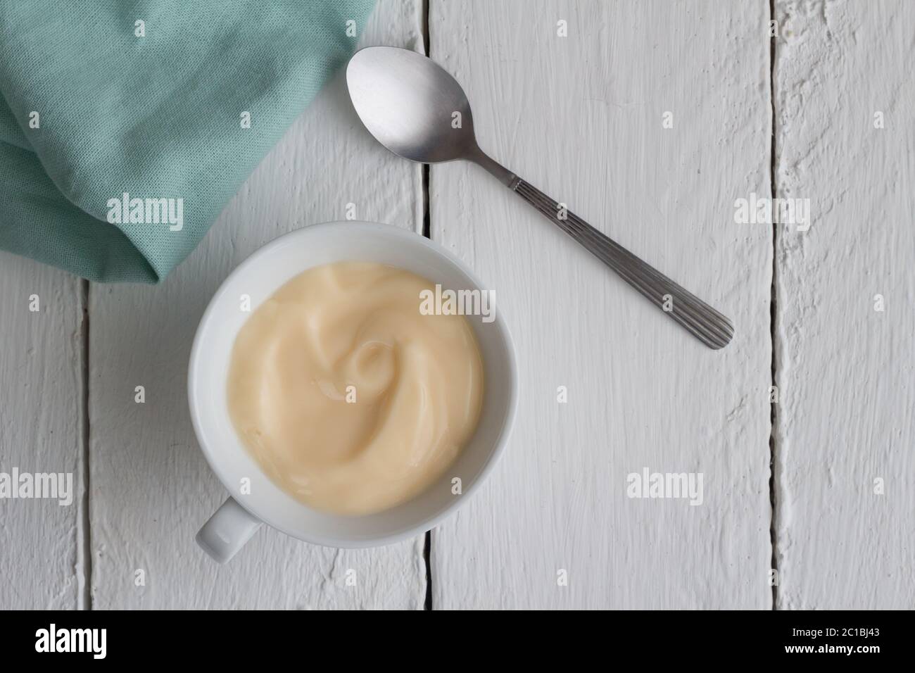 Yogurt in cup on white rustic wooden table background with silver spoon