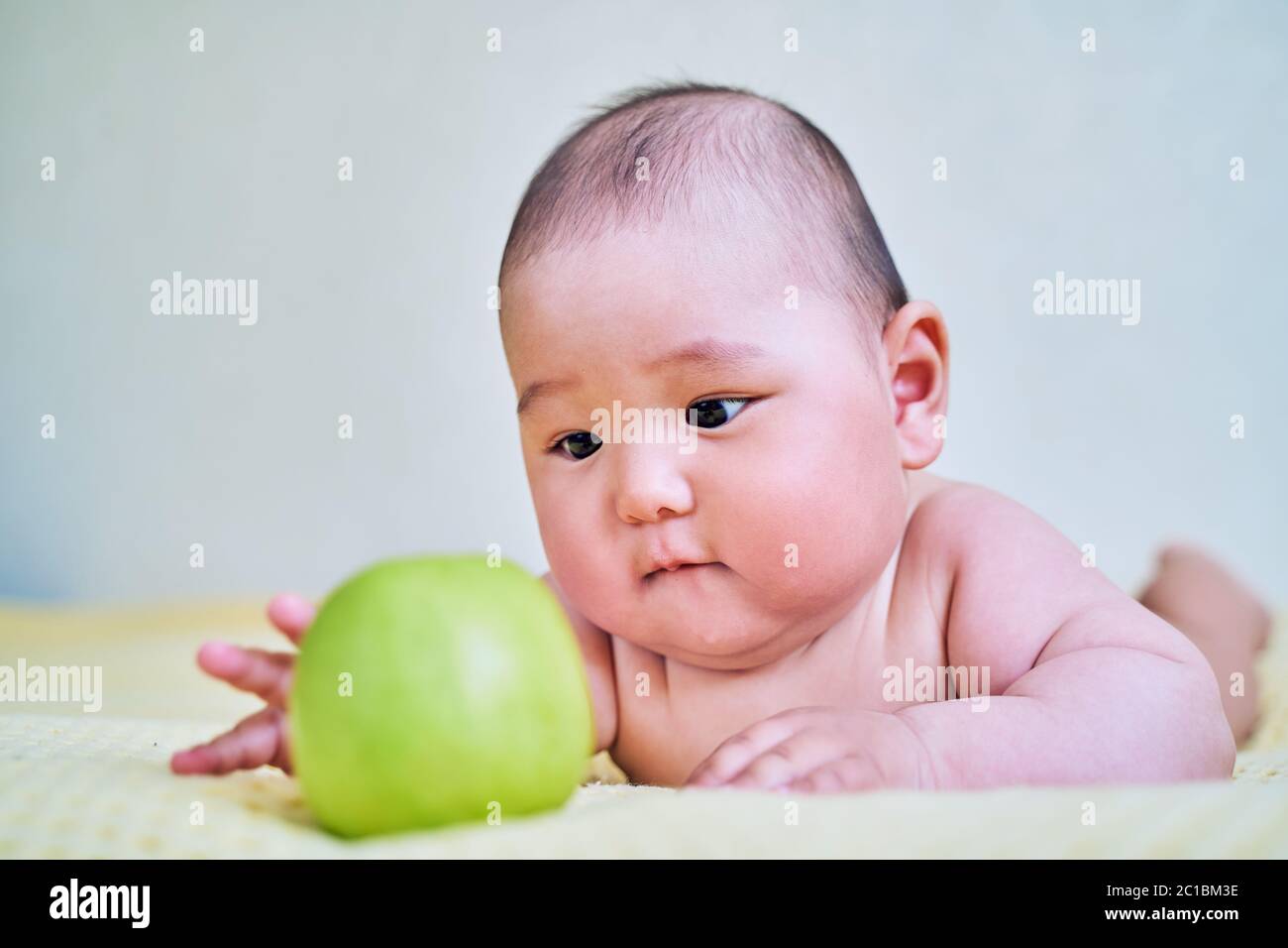 funny Asian kid and green Apple. healthy food for babies Stock Photo