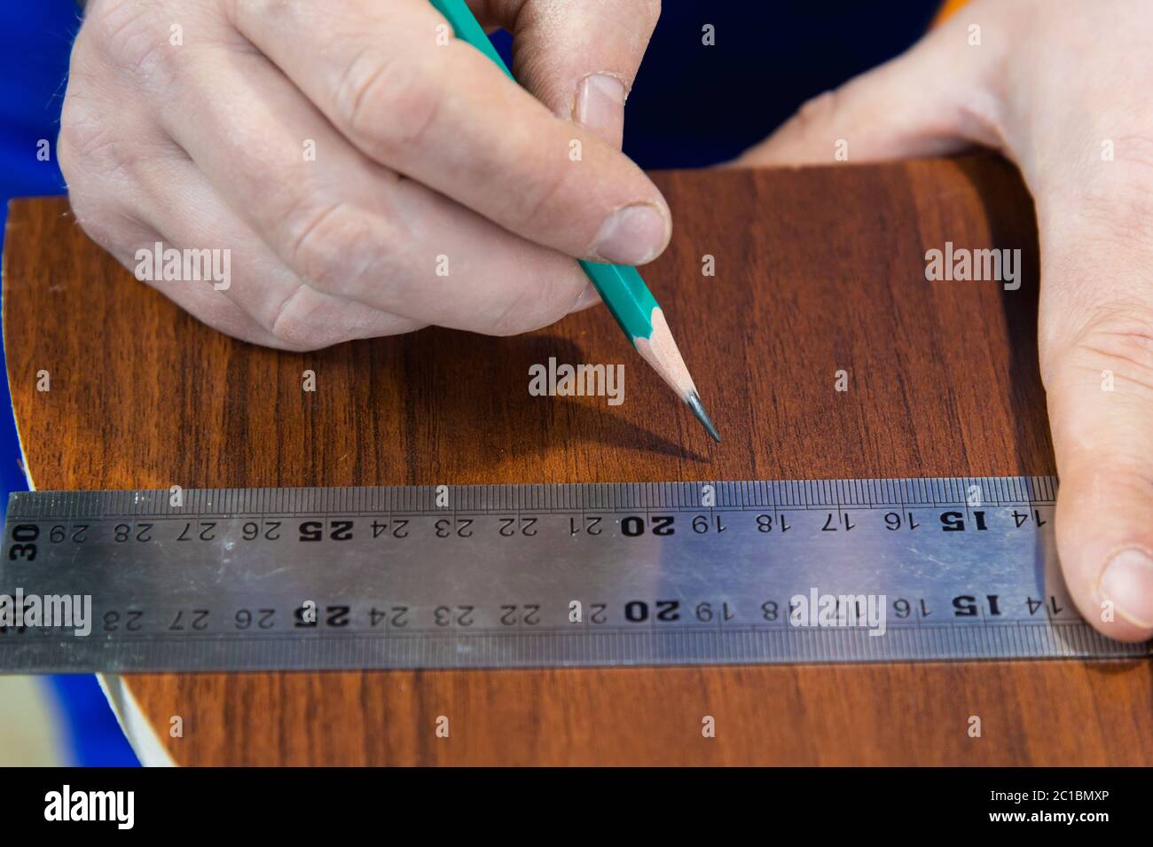 Close-up Men's hands draw a pencil on the ruler with a sub-standard template for cutting out furniture details next to the jigsa Stock Photo