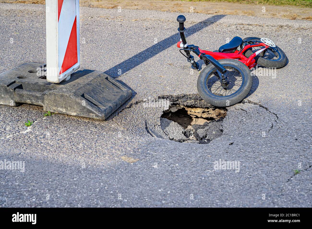 Balance bike (push bike) next to pothole on asphalt street with detour alert traffic sign Stock Photo