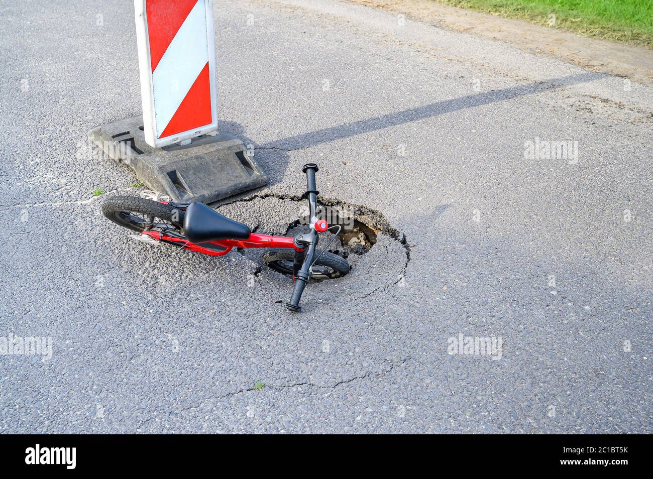 Balance bike (push bike) in pothole on asphalt street with detour alert traffic sign Stock Photo