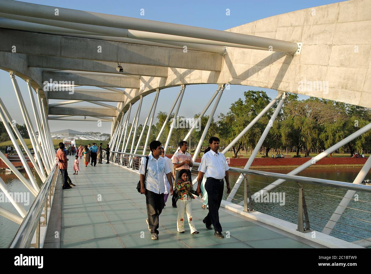 Dhaka in Bangladesh. Jatiya Sangsad Bhaban, the National Parliament House of Bangladesh. People crossing a bridge in the grounds of the building. Stock Photo