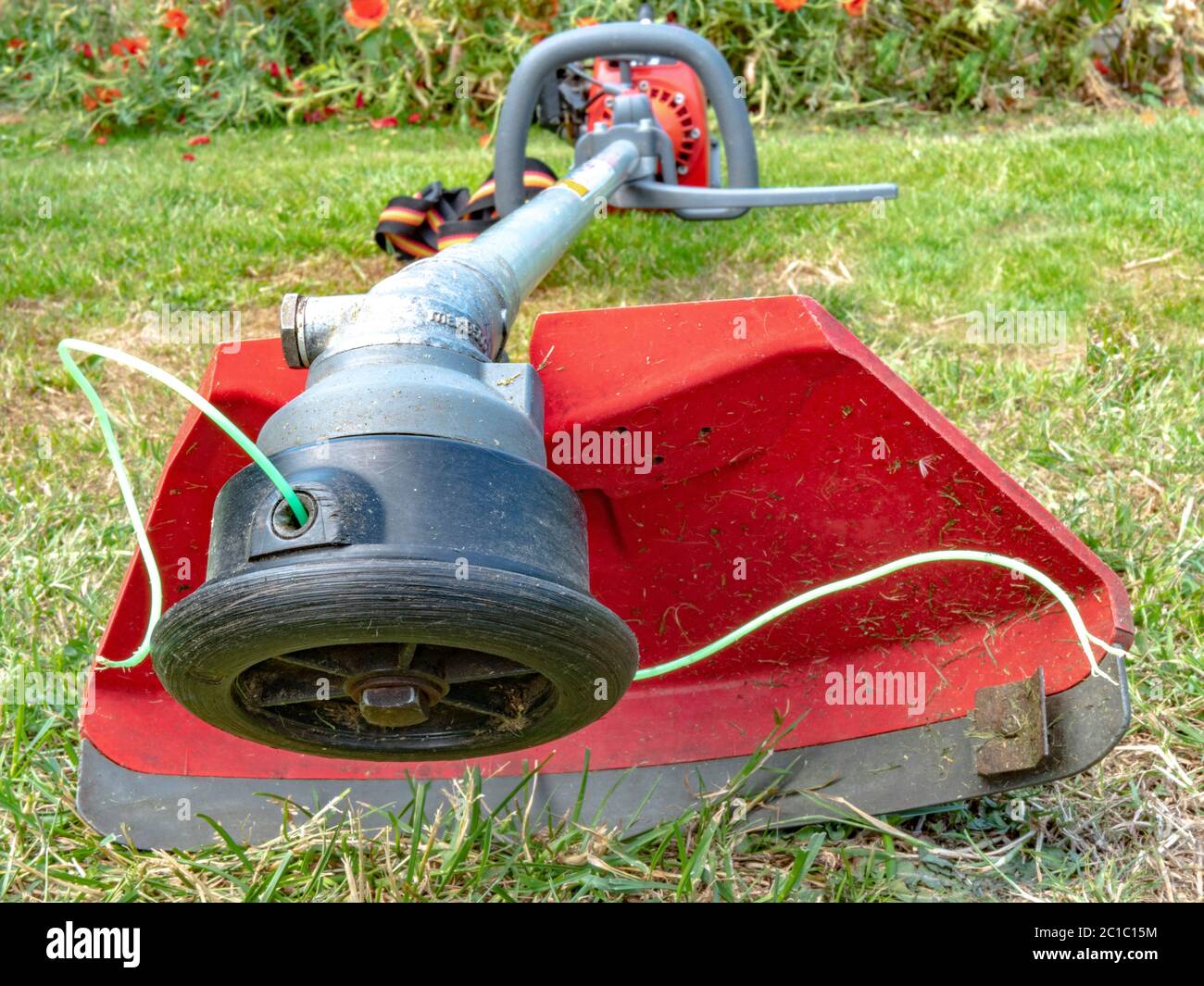 Closeup of the working end of a petrol engine garden strimmer / brush cutter, with exposed nylon line and safety guard, lying on a lawn. Stock Photo