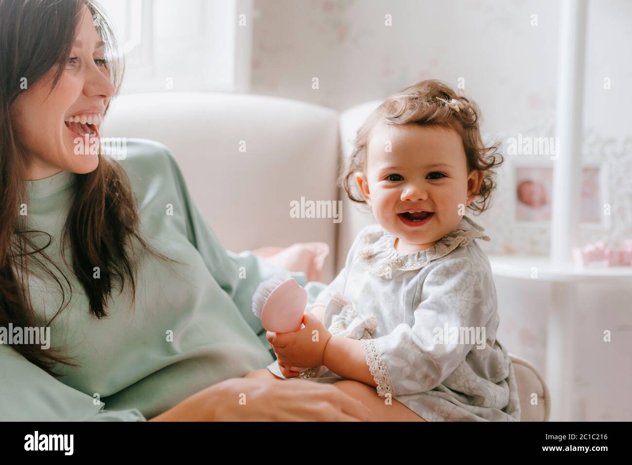 little girl having fun sitting on her pregnant mother in the room Stock Photo