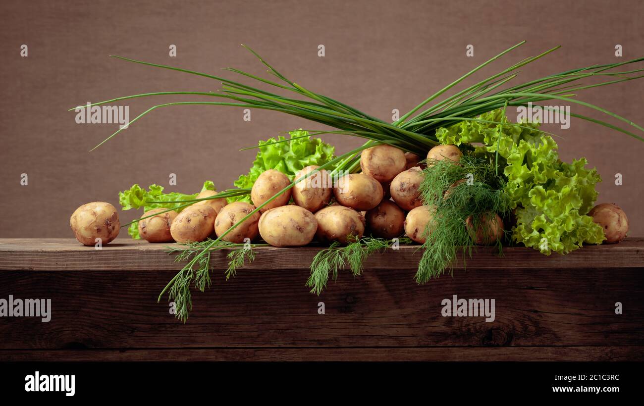 Young fresh organic potatoes with dill, salad and onion on a old wooden table. Copy space. Stock Photo